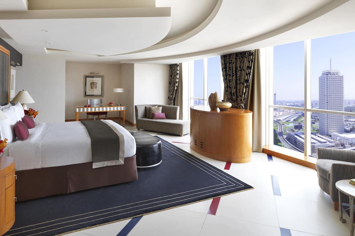 A modern hotel room with a large bed, a desk, a sofa, and a view of the cityscape.