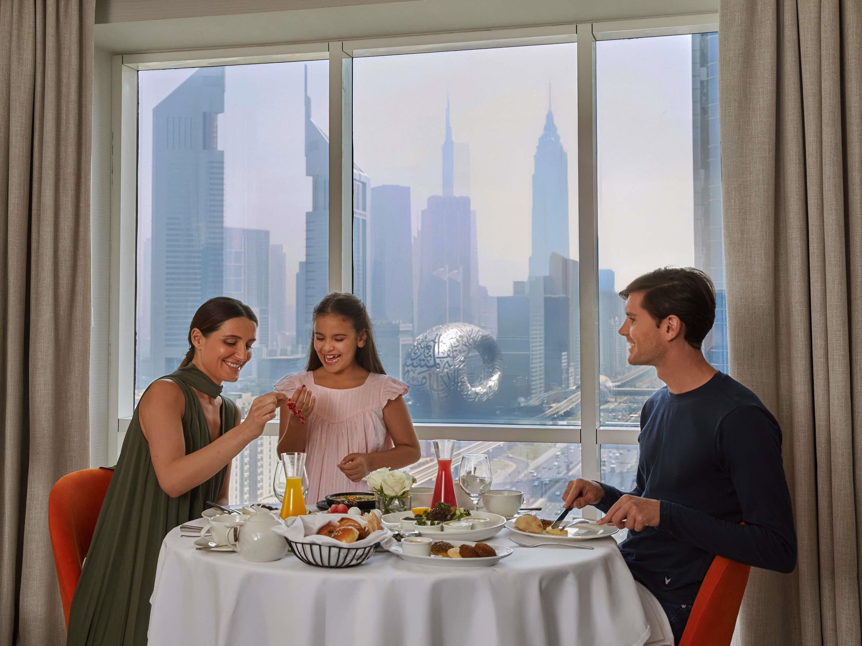 A dining table with breakfast items, a city view, and a window with curtains.