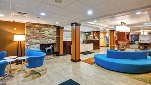 Eine Lobby mit Kamin aus Stein, blauen Sitzgelegenheiten, einem Empfangsbereich und einem Essbereich.