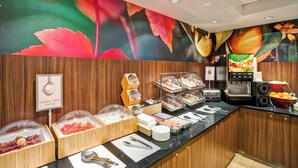 Ein Frühstücksbuffet mit verschiedenen Speisen, darunter Obst, Joghurt und einer Kaffeemaschine.