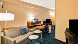 Ein Hotelzimmer mit einer Couch, zwei kleinen Tischen, einem Schreibtisch mit Computer, einem Fernseher und einer Lampe.