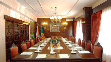 Un salón de conferencias con una larga mesa, sillas, una lámpara de araña y una bandera.