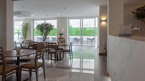 A spacious indoor area with multiple wooden tables and chairs, large windows offering a view of greenery outside, and a marble reception desk. - Hotel Afonso V (Aveiro)