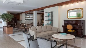 A spacious lobby with a sofa, chairs, a coffee table, a piano, and a bar area with shelves of bottles. - Hotel Afonso V (Aveiro)