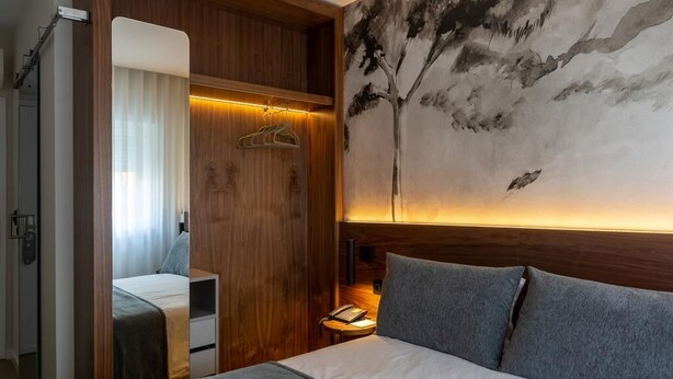 A hotel room with a bed, a wooden wardrobe, a nightstand, and a wall painting. - Hotel Afonso V (Aveiro)