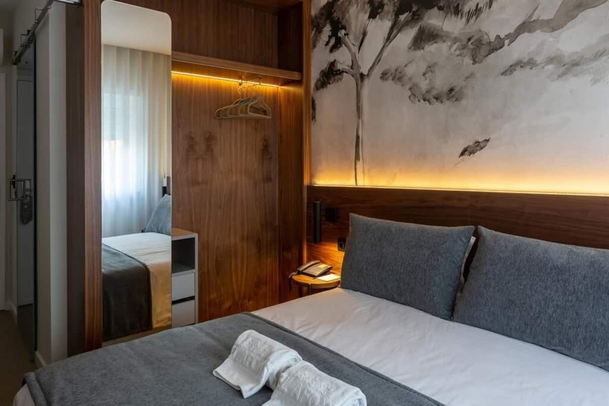 Habitación de hotel con una cama, un armario de madera, una mesita de noche y un cuadro en la pared.