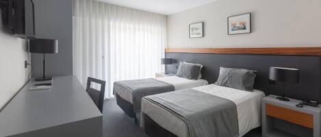 A hotel room with two beds, a desk, a chair, a TV, and two framed pictures on the wall.