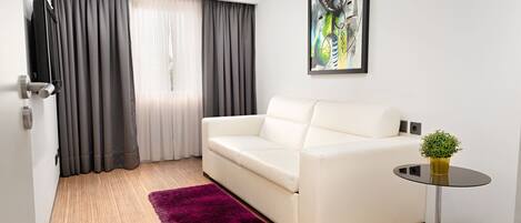 Una sala de estar moderna con un sofá blanco, un tapete púrpura, una pequeña mesa redonda con una planta y un cuadro en la pared.