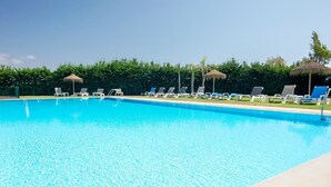 A clear blue swimming pool with lounge chairs and umbrellas along the edge. - Hotel dos Zimbros (Sesimbra)