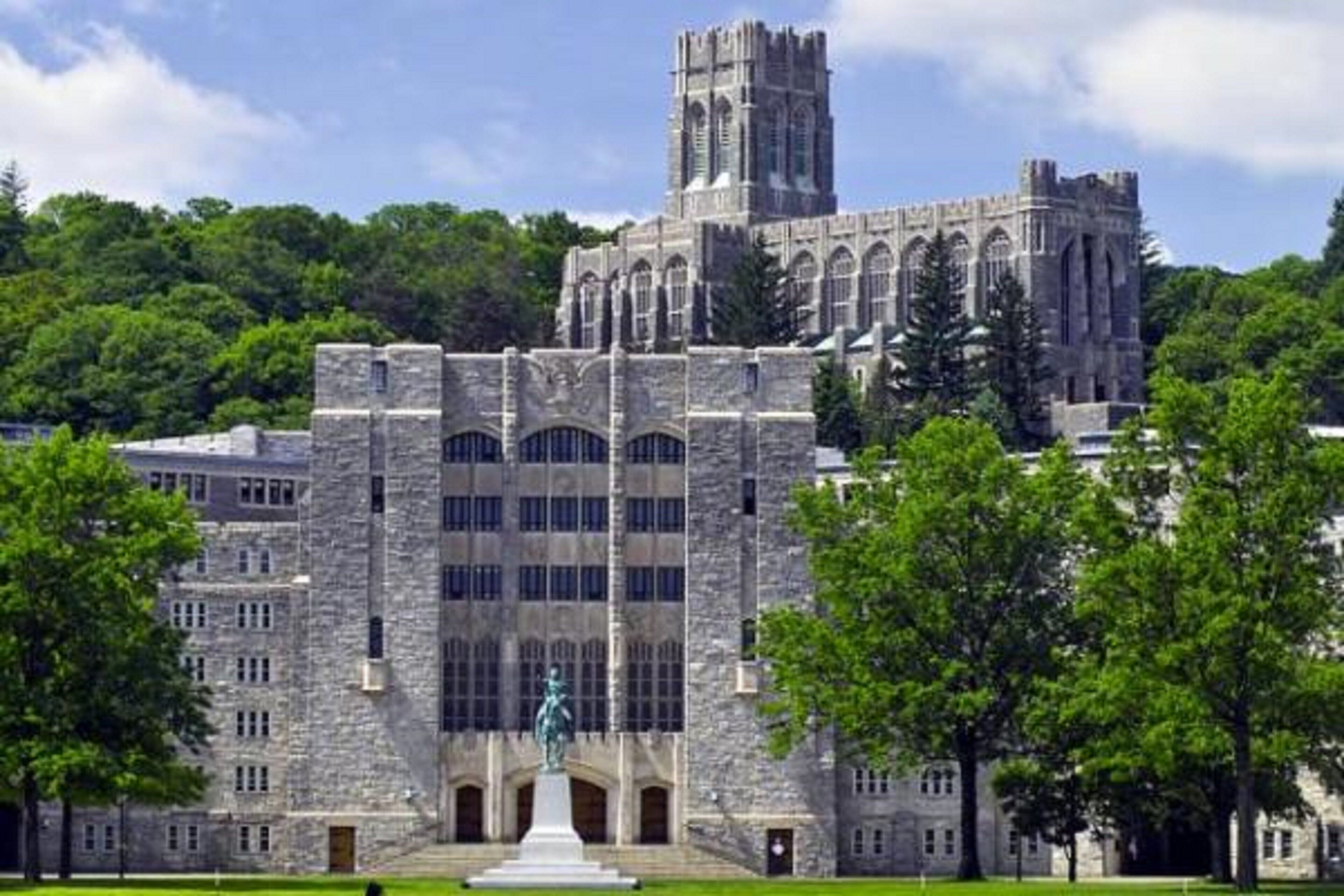 A historic stone building with a central tower, large windows, and a statue in front.