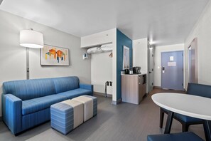 Een moderne hotelkamer met een blauwe bank, een witte tafel en een kitchenette.