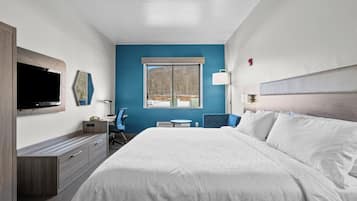 A hotel room with a large bed, a TV mounted on the wall, a desk with a chair, and a window with a view of trees.
