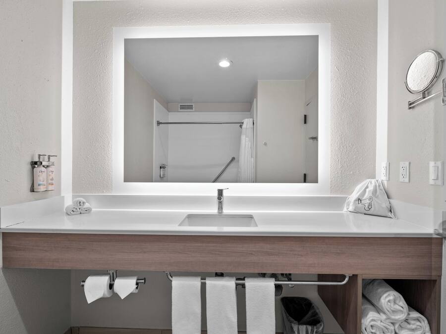 A bathroom with a white sink, a mirror, a towel rack, and a shower visible in the reflection.