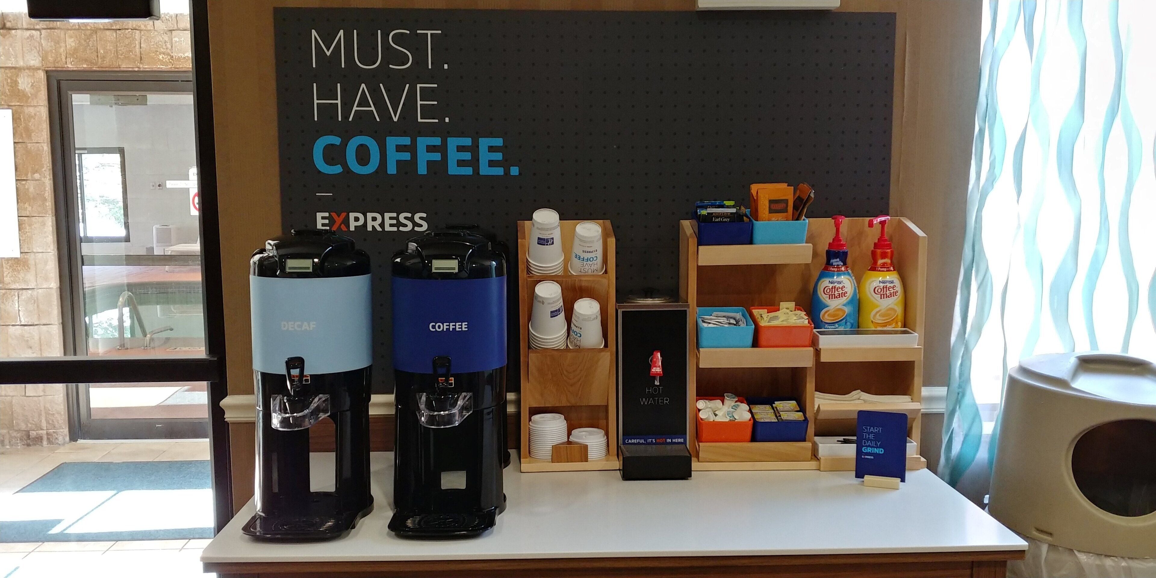 Una estación de café con dos dispensadores de café, un cartel que dice 'MUST. HAVE. COFFEE. EXPRESS' y una exhibición de artículos relacionados con el café.