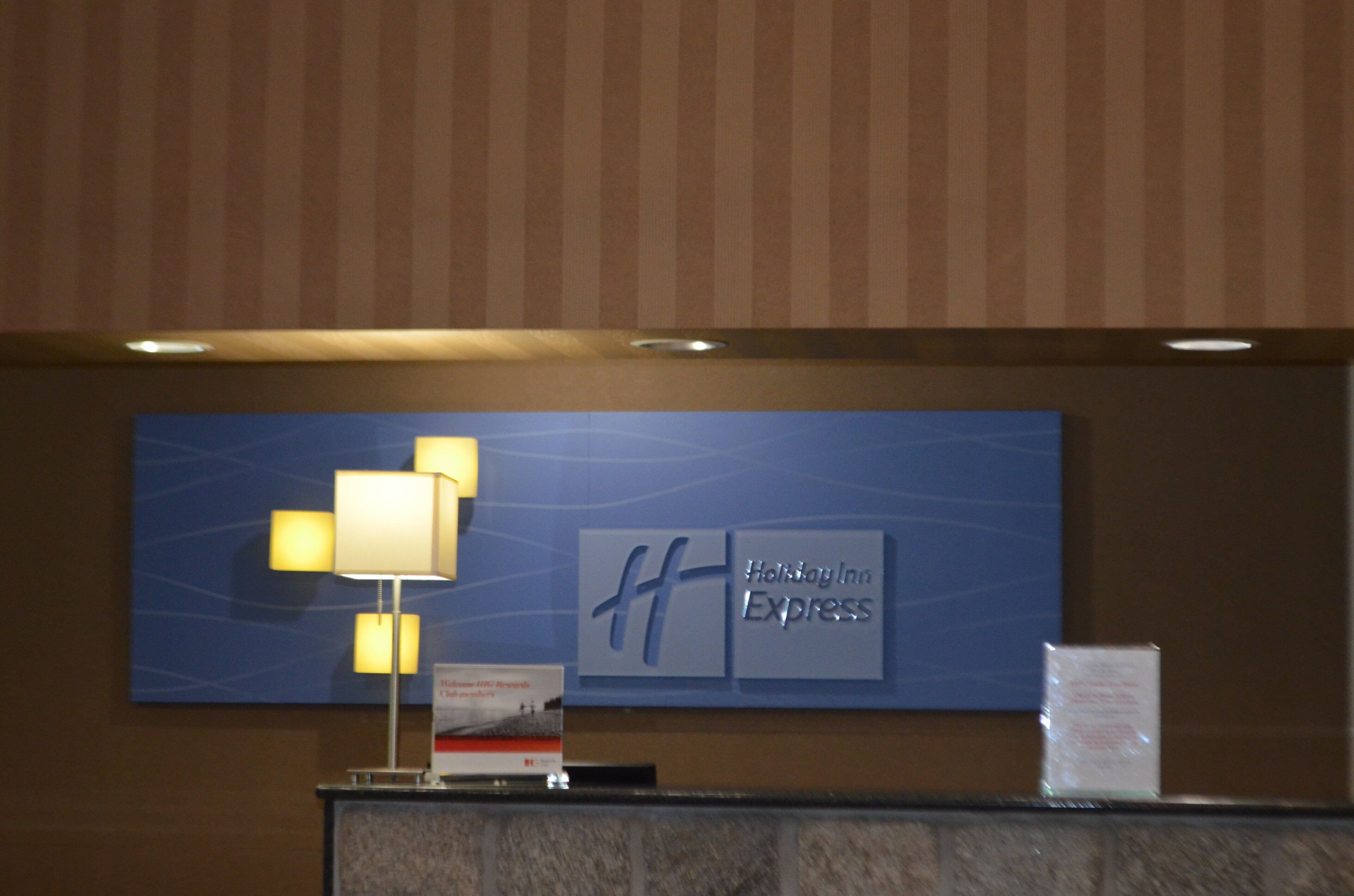 A reception desk with a Holiday Inn Express sign, a lamp, and a small informational sign.