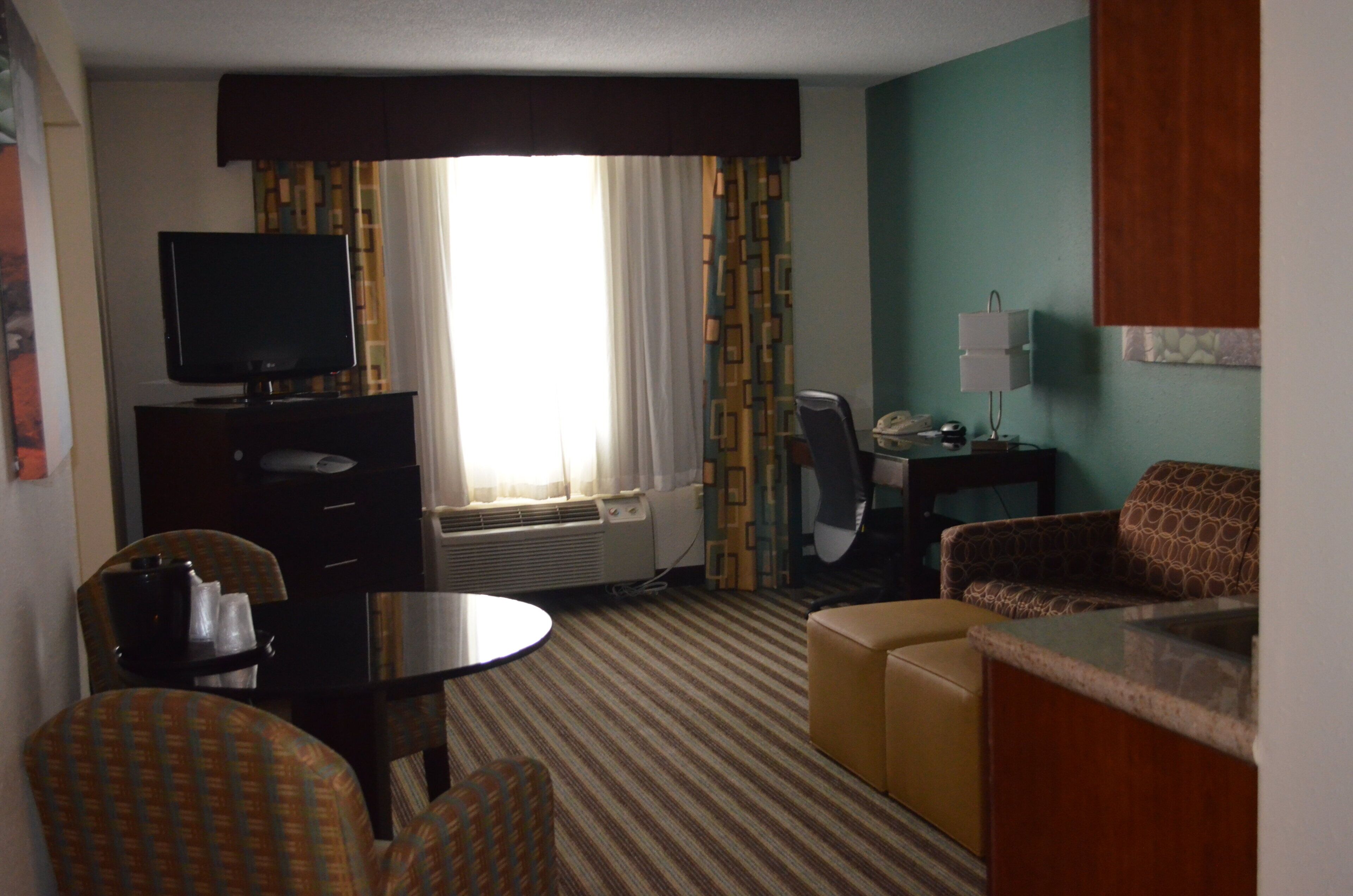 Una habitación de hotel con televisión, escritorio, silla, sofá y ventana con cortinas.
