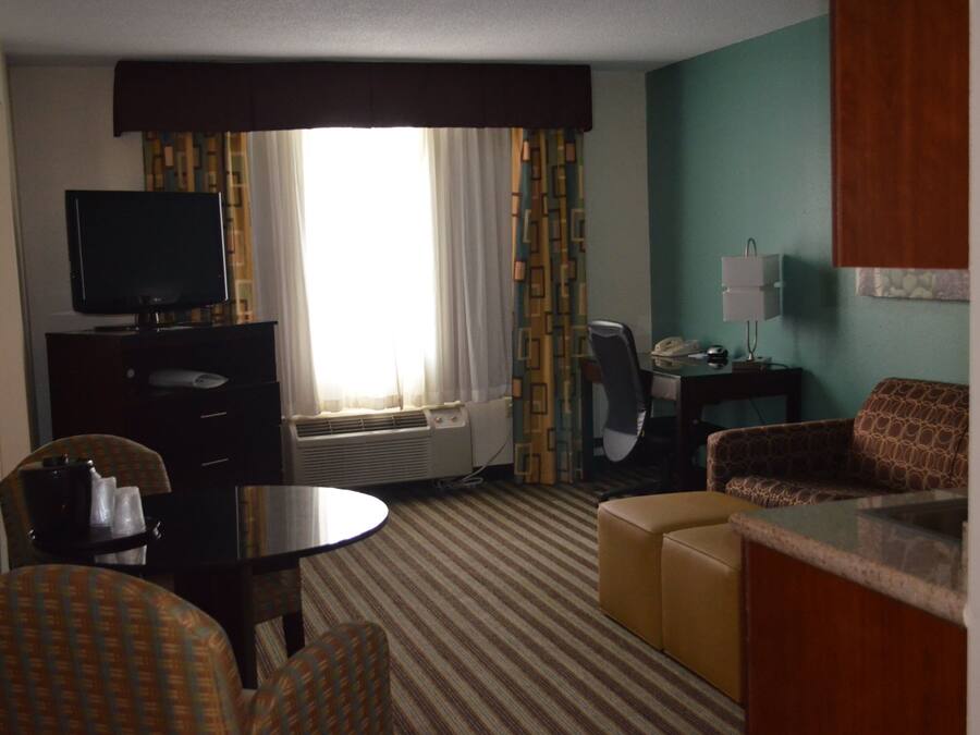 Una habitación de hotel con televisión, escritorio, silla, sofá y ventana con cortinas.