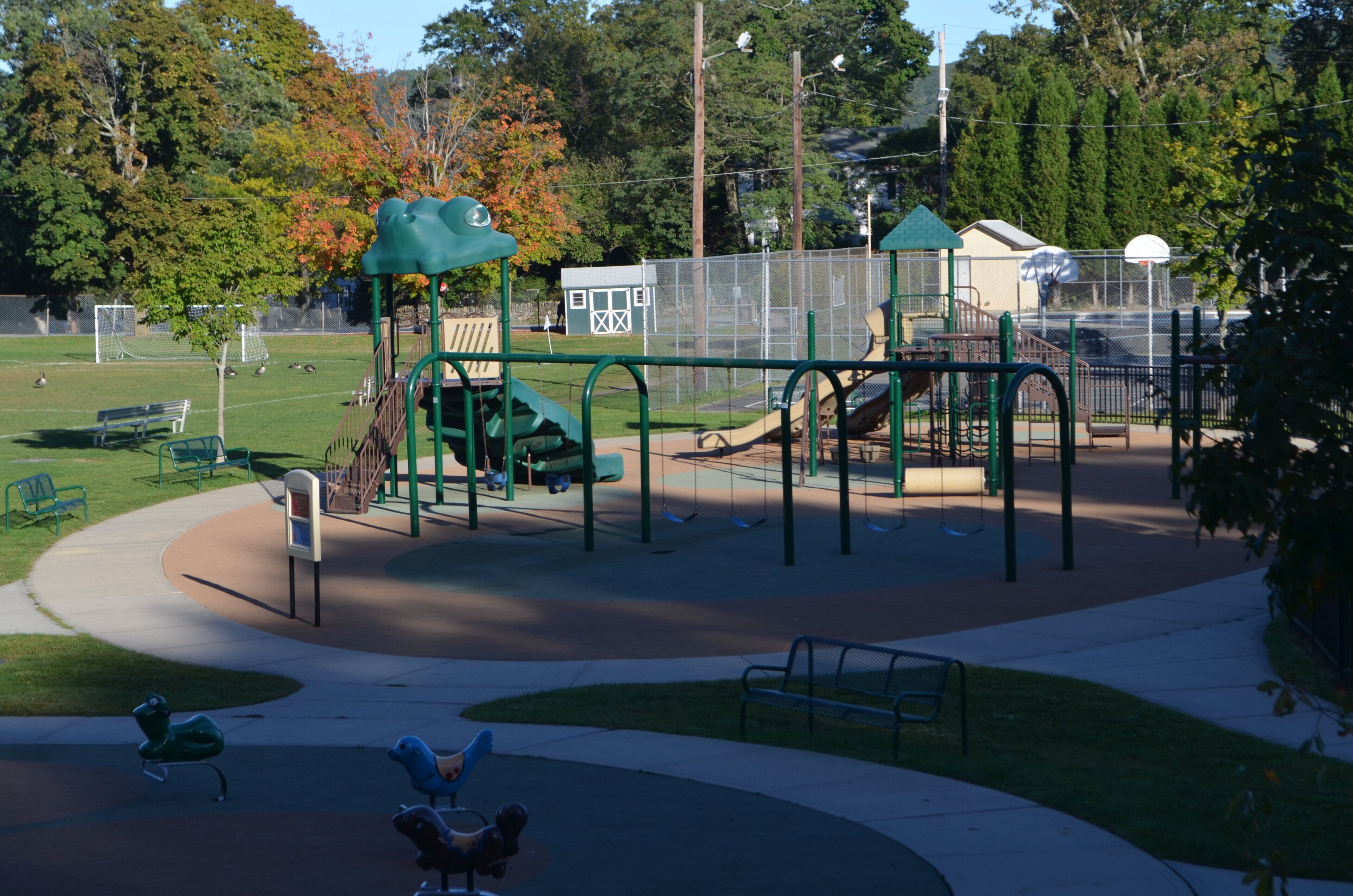 Un parque infantil con diversas estructuras de juego, una banca y una zona cercada.