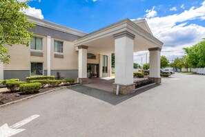 A hotel entrance with a covered porch, a driveway, and a parking area.