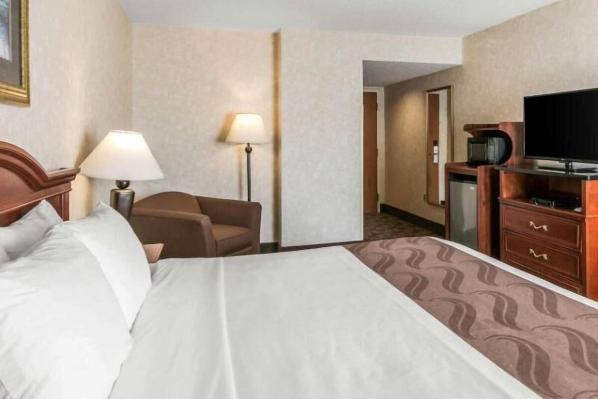 A hotel room with a bed, a desk, a chair, a television, and a lamp.