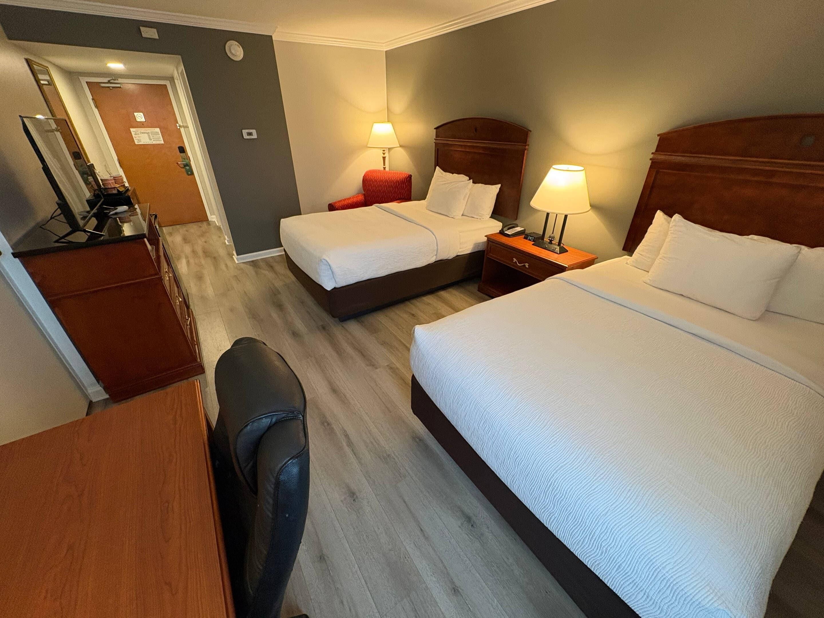 A hotel room with two beds, a desk, a chair, and a mirror.