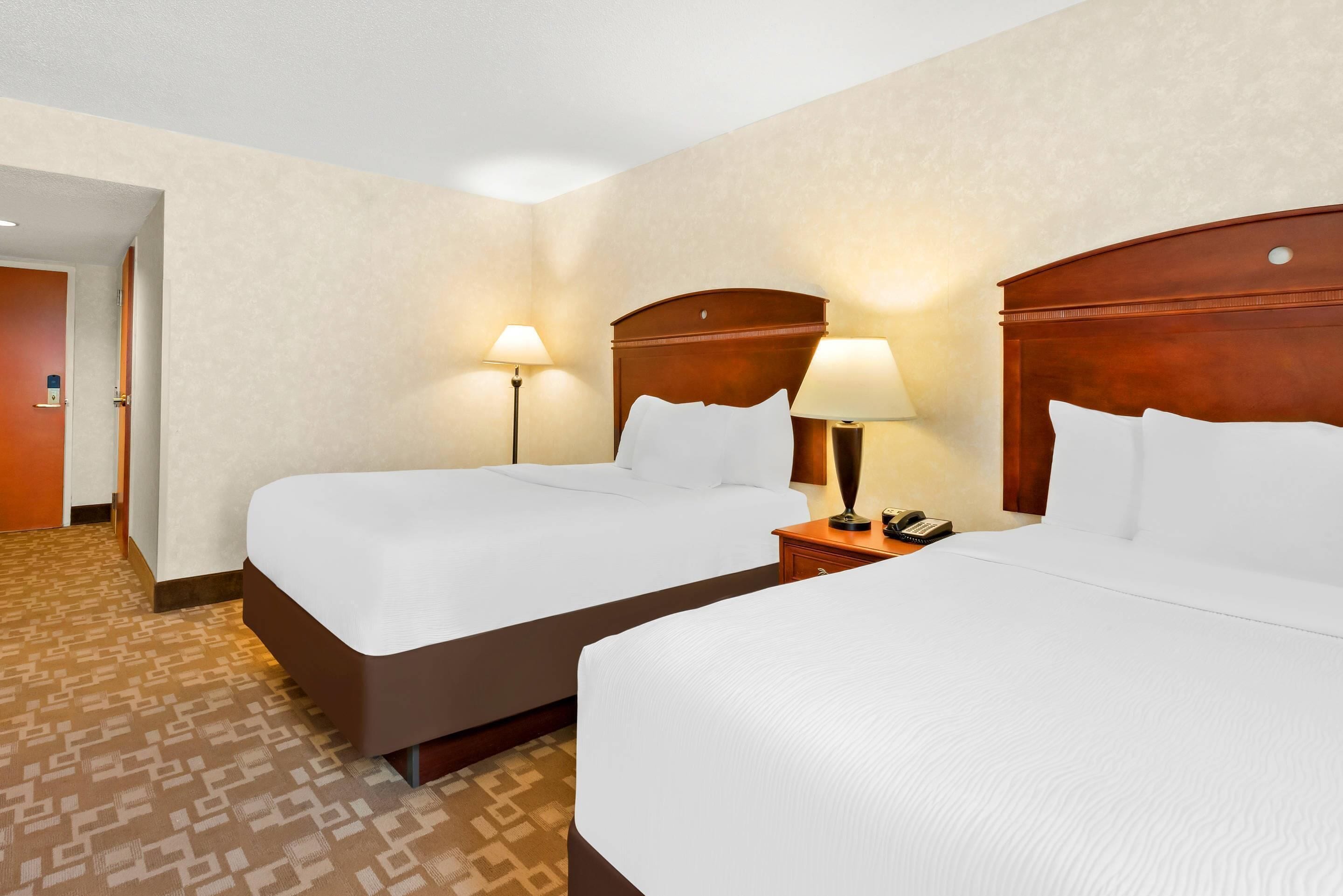 A hotel room with two beds, a wooden headboard, bedside lamps, and a patterned carpet.