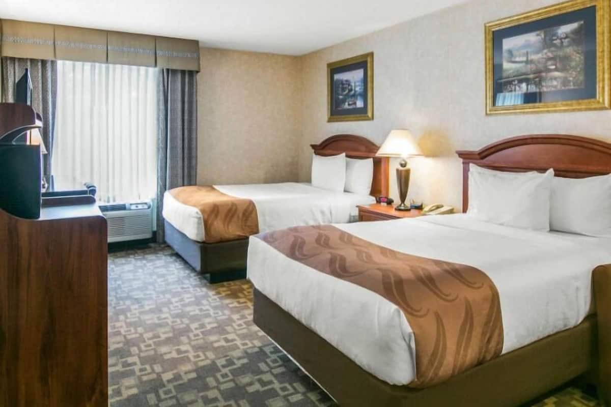 A hotel room with two beds, a desk with a lamp, a telephone, and a window with curtains.
