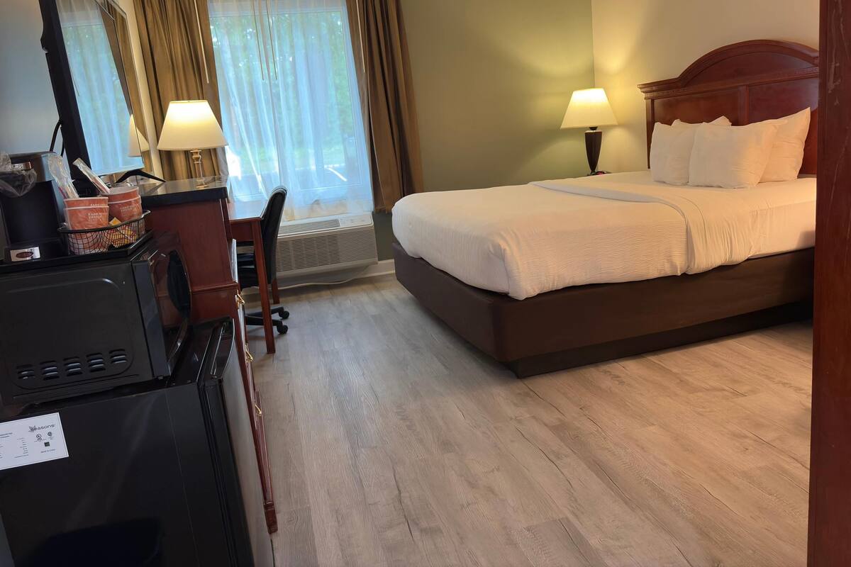 A hotel room with a bed, desk, chair, and a large window with curtains.