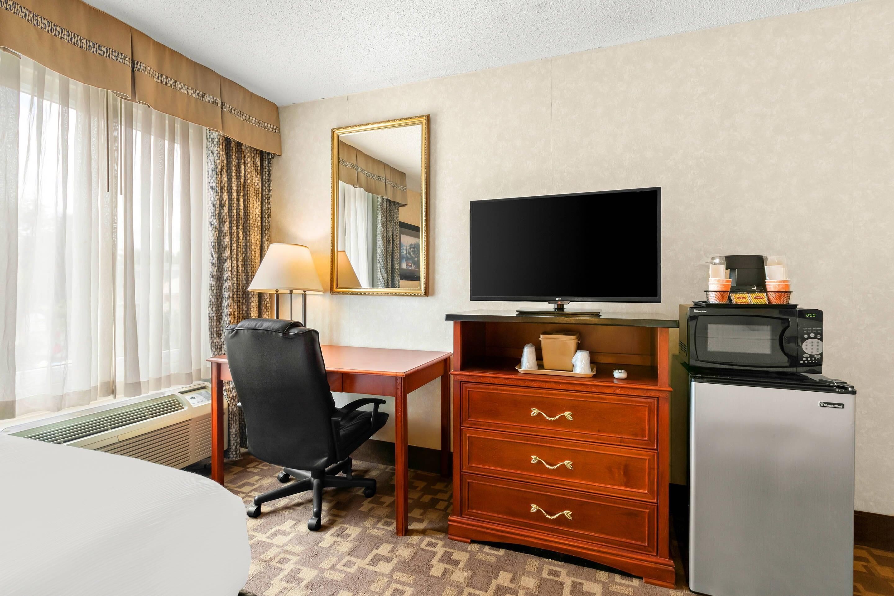 Habitación de hotel con cama, escritorio, silla, televisor, refrigerador y microondas.