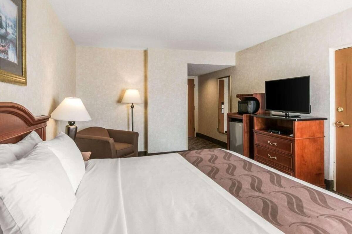 A hotel room with a bed, a desk with a television, a lamp, and a chair.