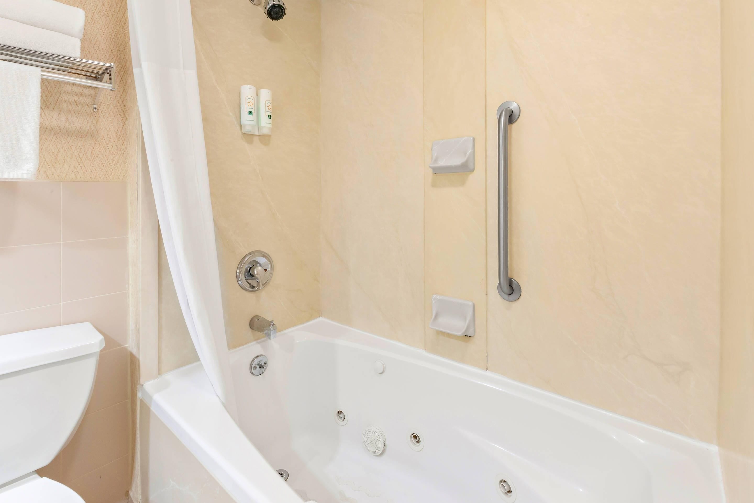 A bathroom with a bathtub, a toilet, a shower curtain, and a handrail.