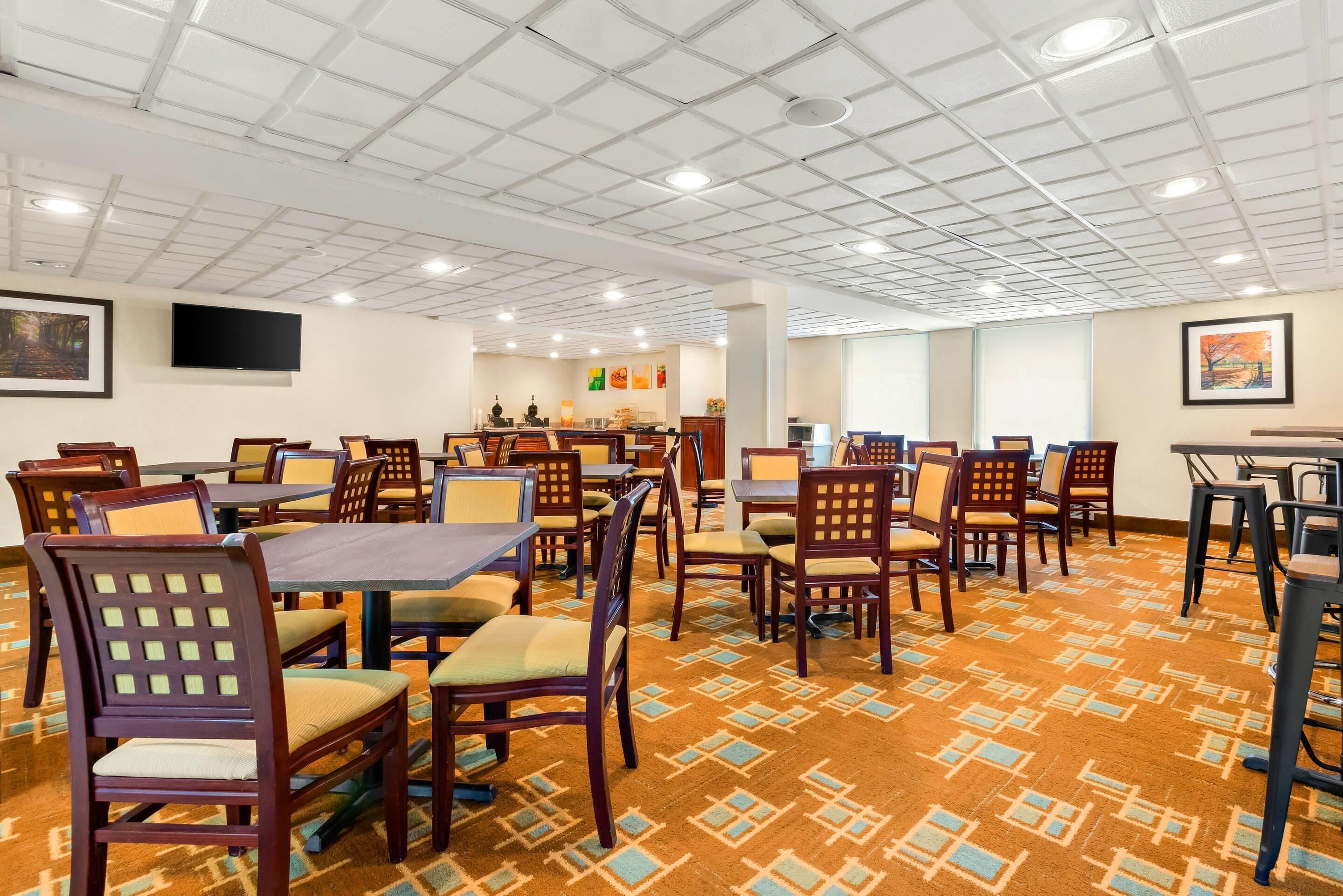 Une salle à manger d’hôtel avec plusieurs tables et chaises, un téléviseur à écran plat fixé au mur et une moquette à motifs.