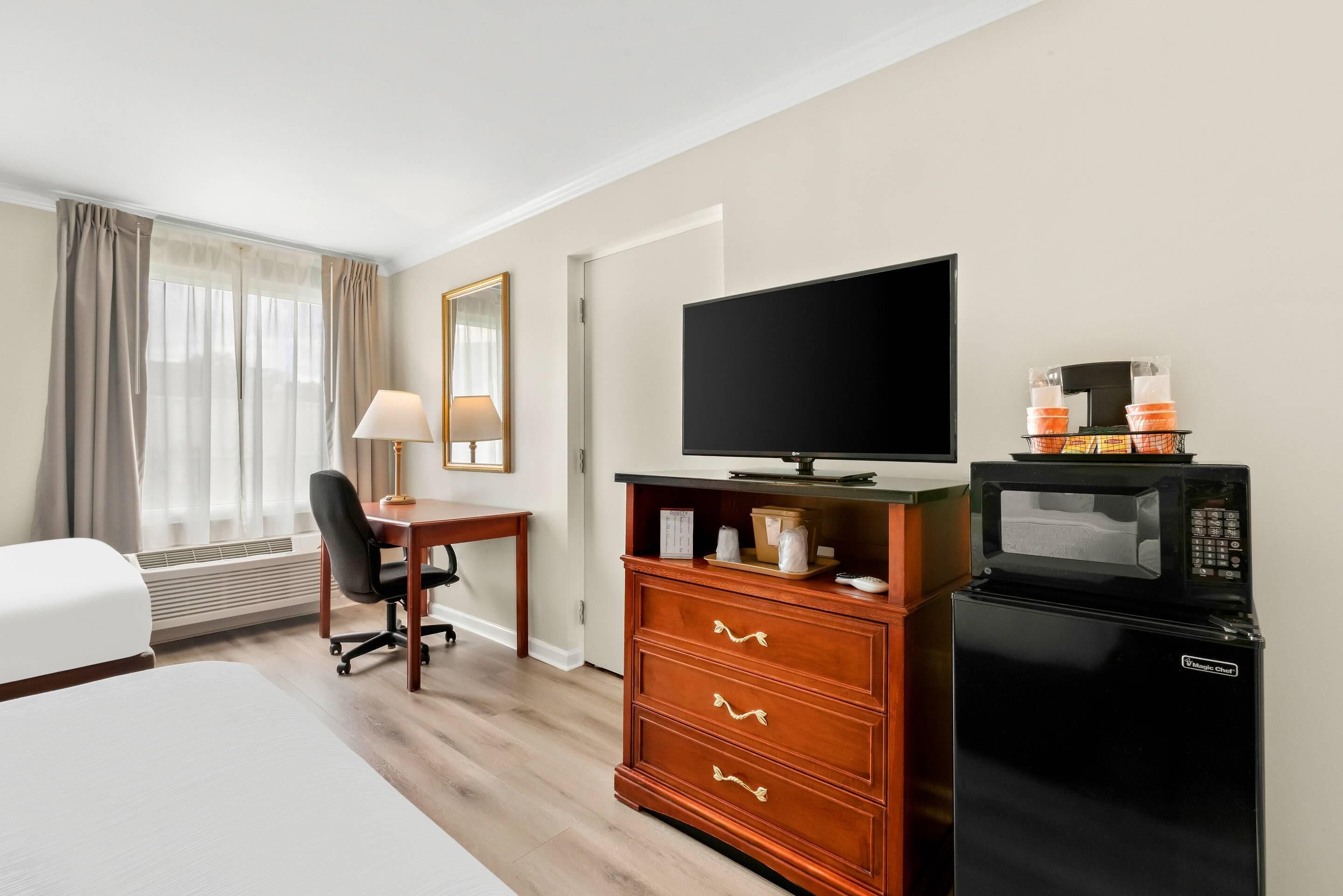 A hotel room with a bed, desk, television, minibar, and a window with curtains.