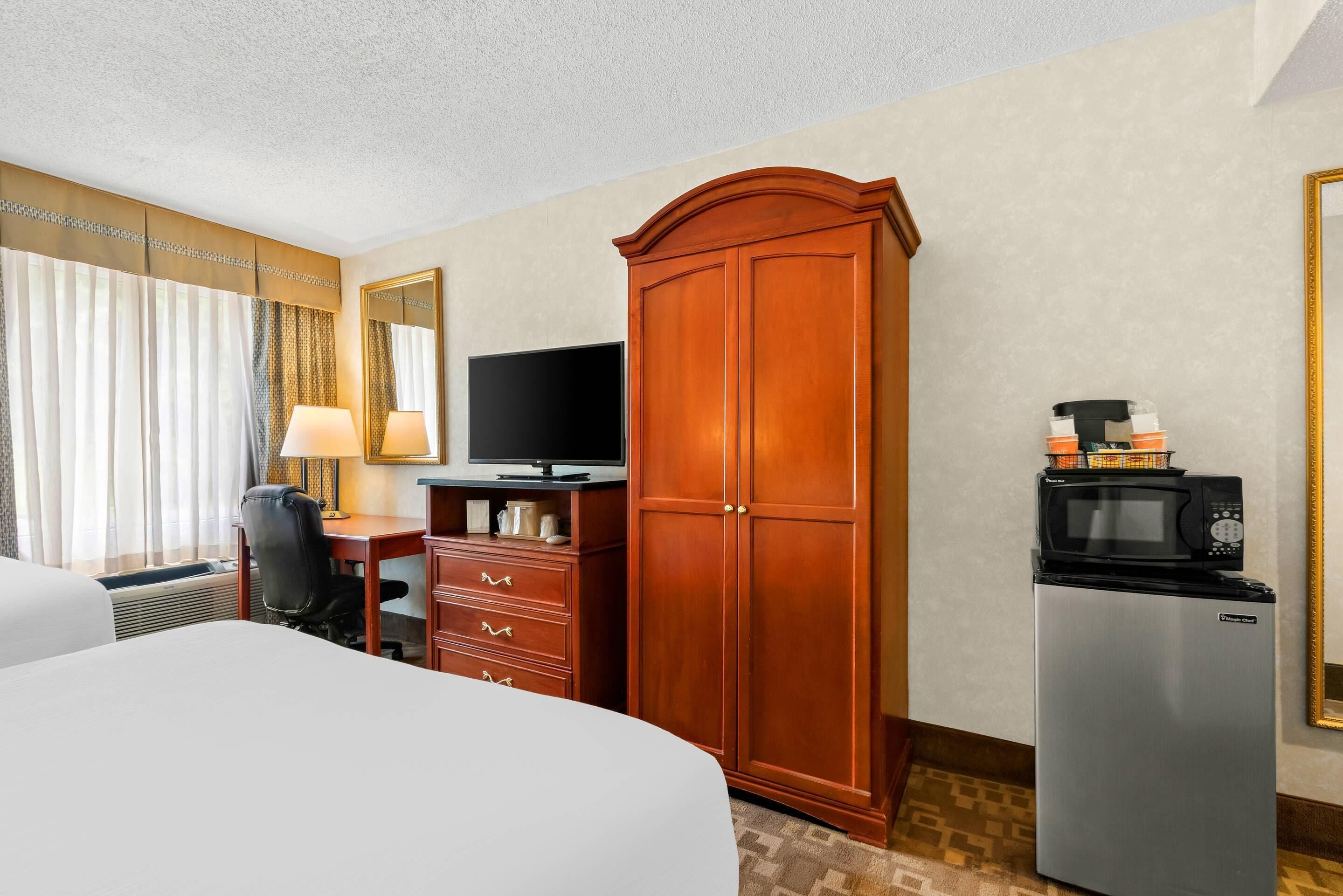 A hotel room with a bed, a desk with a computer, a wardrobe, a television, and a refrigerator.