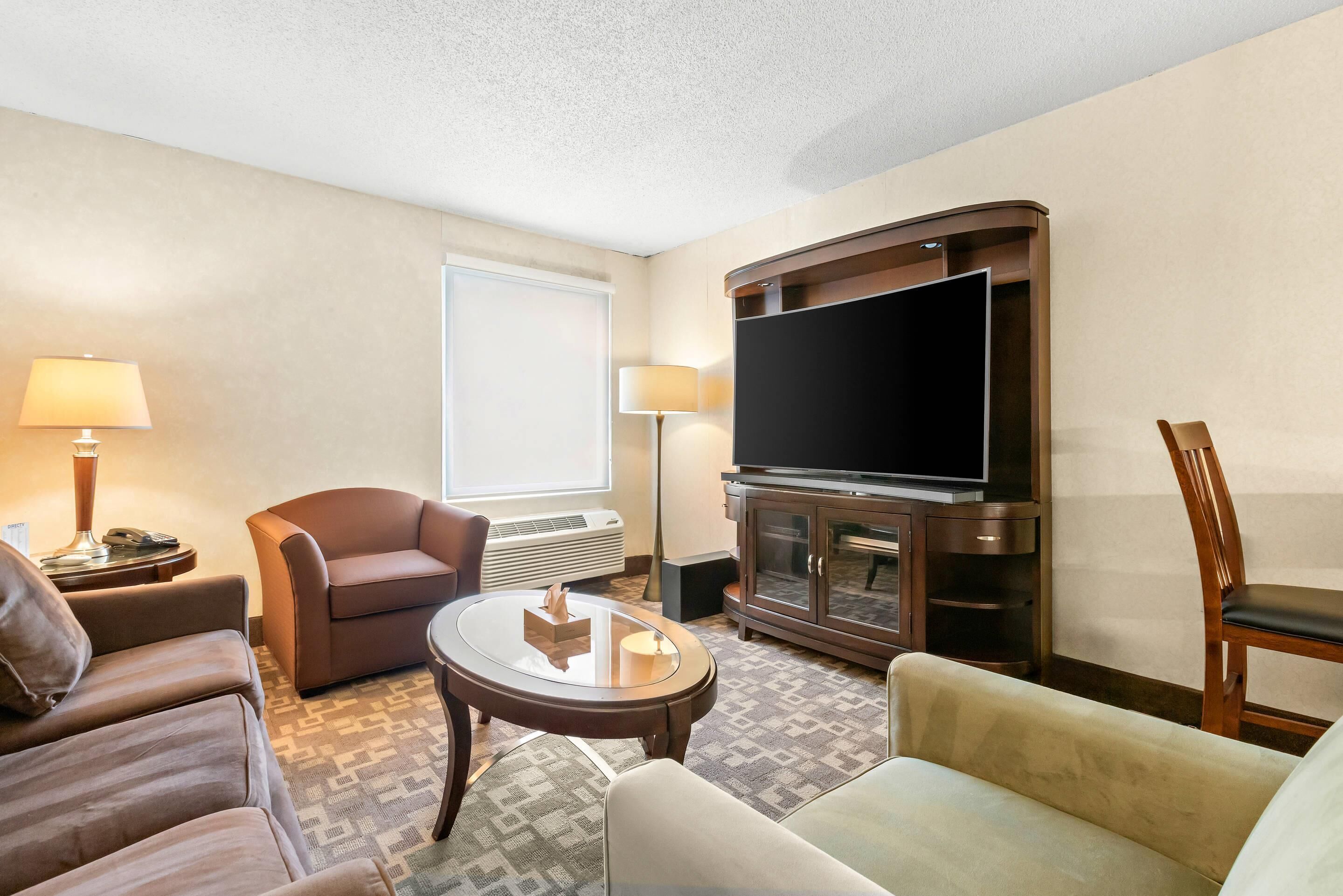 Une chambre d’hôtel équipée d’un téléviseur à écran plat, d’un canapé, d’un fauteuil, d’une petite table et d’une lampe.