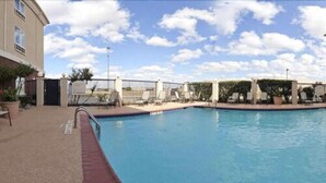 Una piscina con zona de terraza cercada, sillas de descanso y cielo despejado.