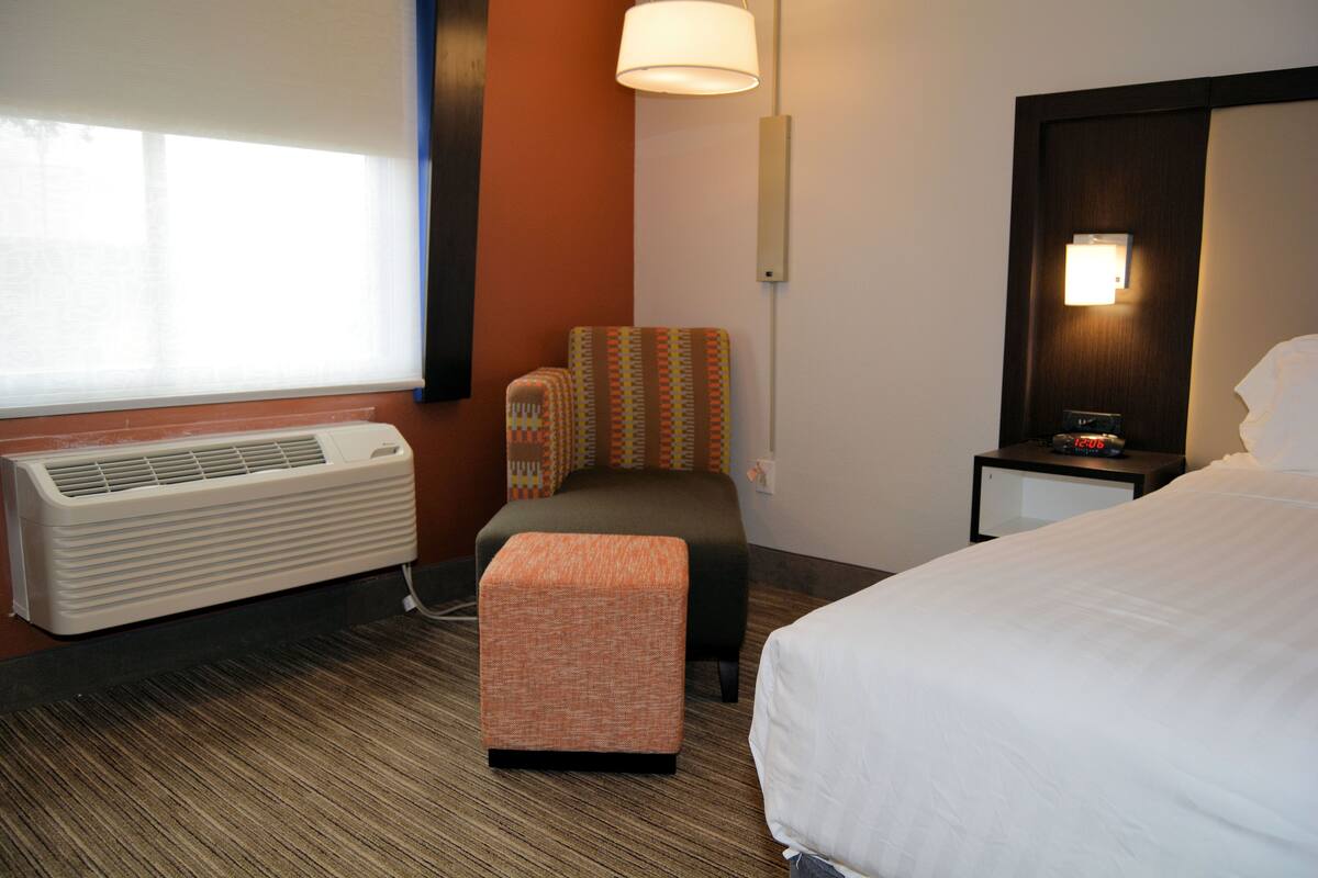Ein Hotelzimmer mit einem Bett, einem kleinen Tisch mit Lampe, einem Sessel, einem Heizgerät und einem Fenster mit Jalousien.
