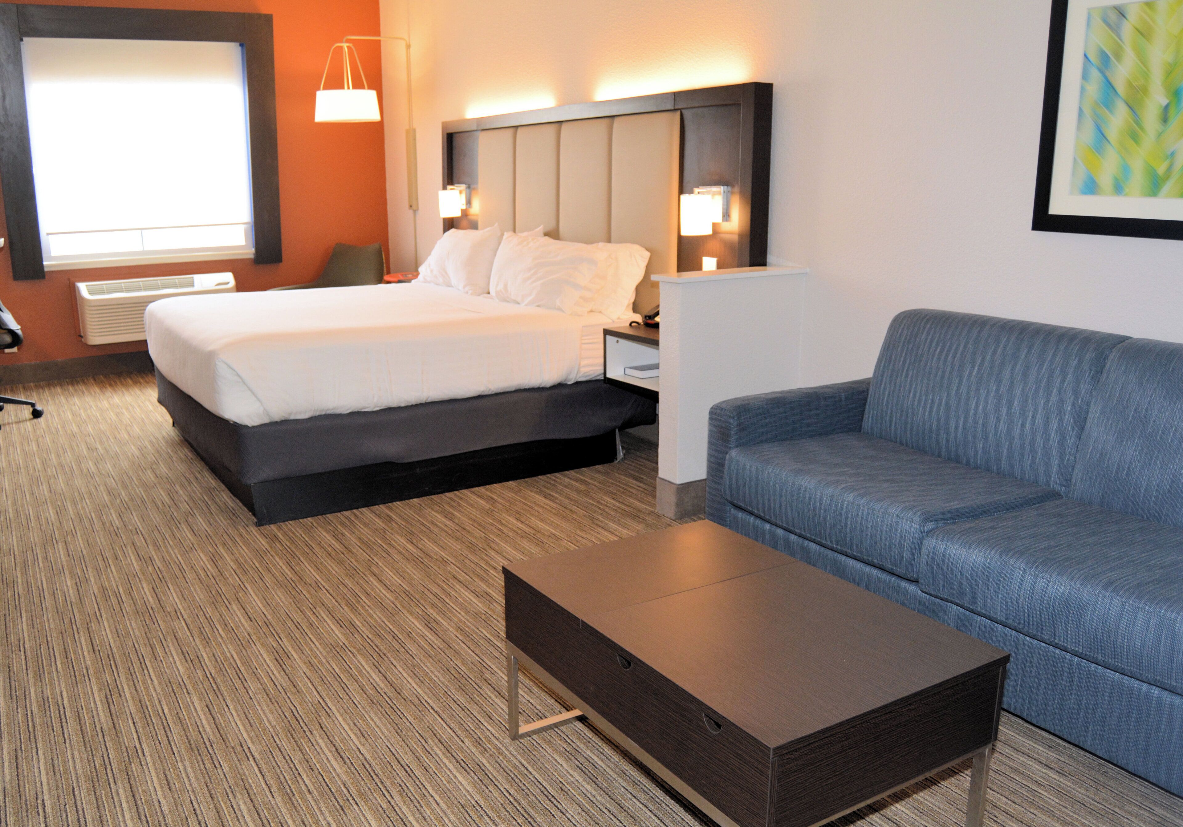 A hotel room with a bed, a sofa, a nightstand, a lamp, and a window.