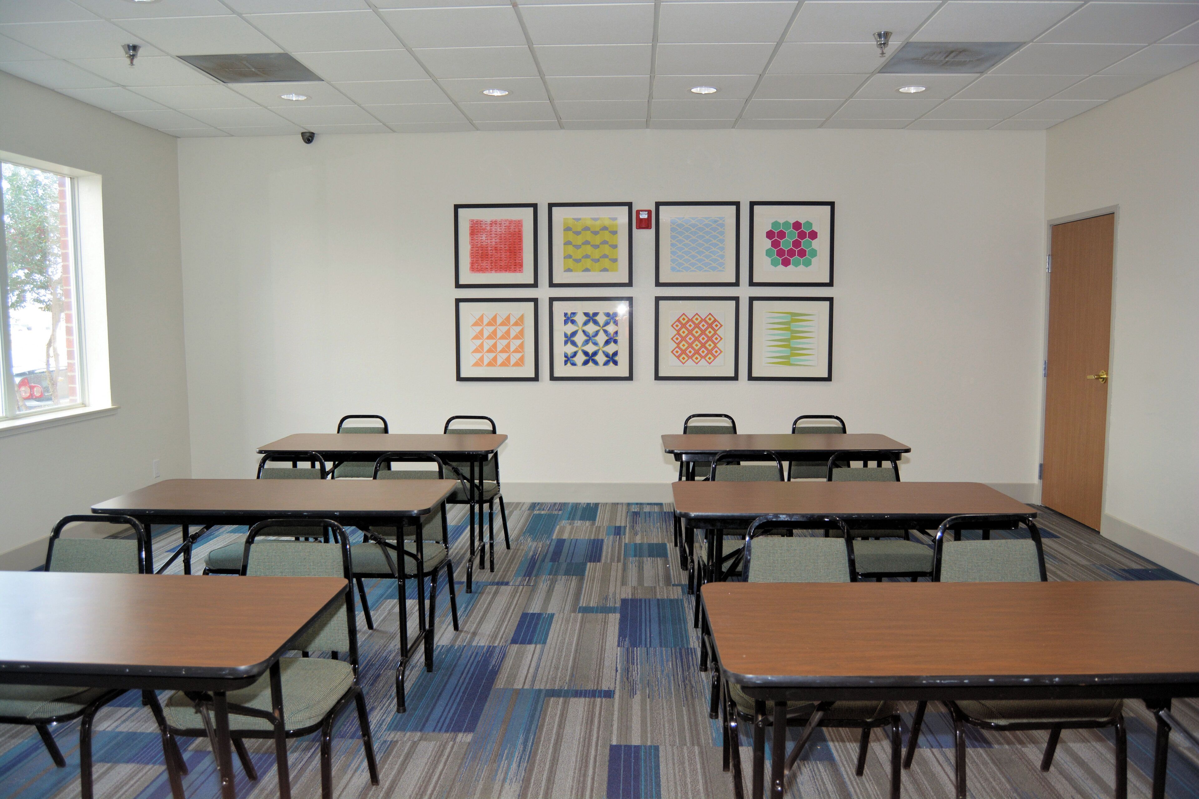 A conference room with six tables, chairs, and a wall with framed geometric patterns.