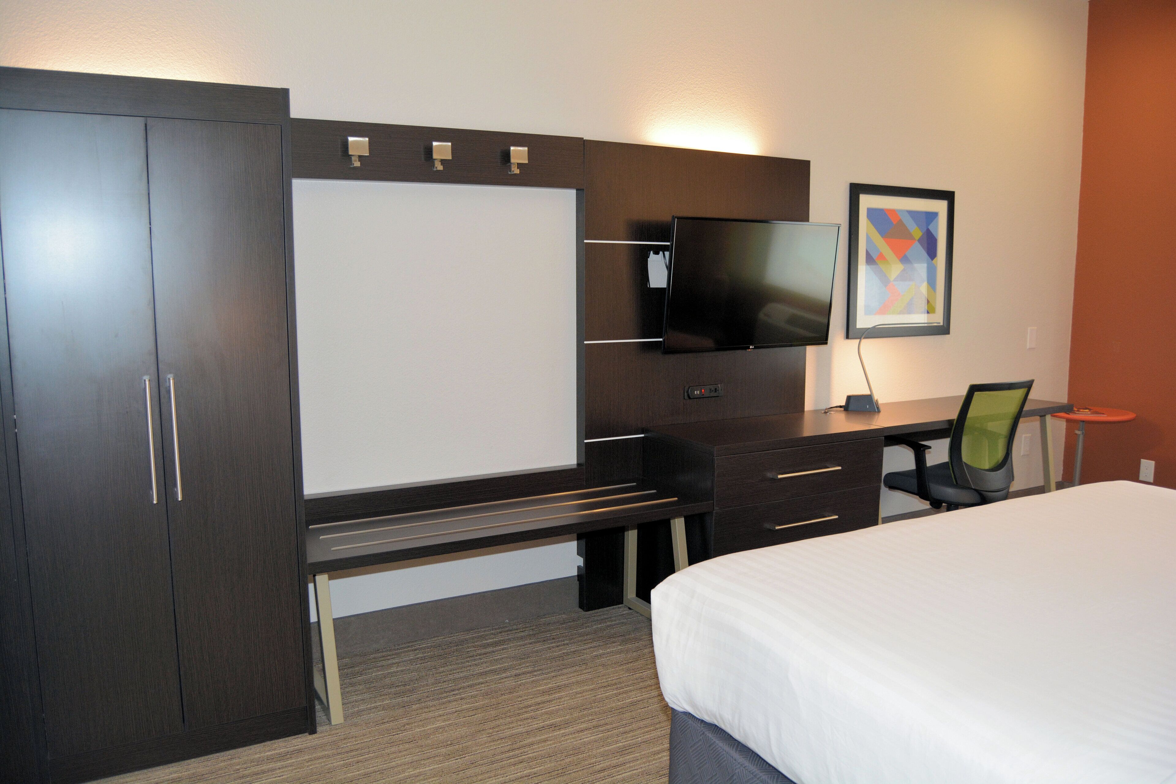 Une chambre d’hôtel avec un lit, un bureau, une chaise, une télévision et un tableau encadré au mur.