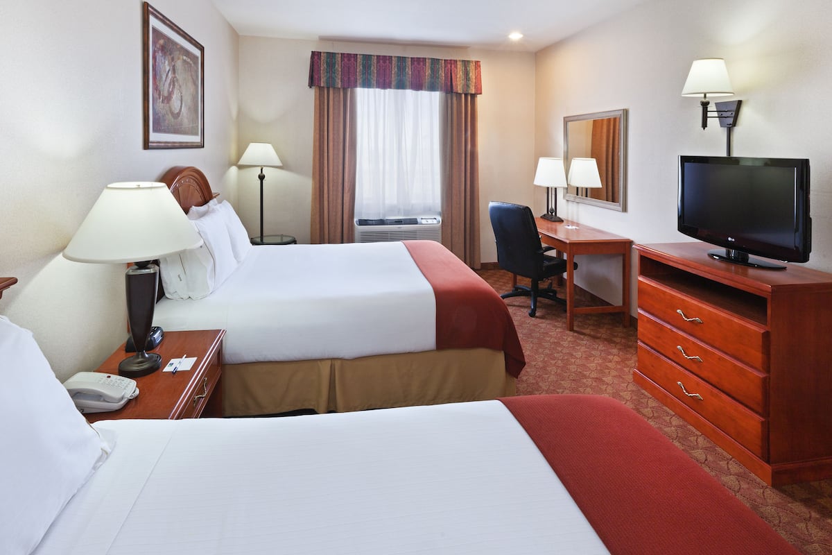 Ein Hotelzimmer mit zwei Betten, einem Schreibtisch mit Stuhl, einem Fernseher und einer Schreibtischlampe.