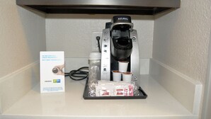 Una cafetera Keurig con un recipiente de goteo, cápsulas de café y una taza de café con la marca Keurig.