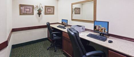 Una oficina de hotel con un escritorio, dos sillas, una computadora y un espejo grande.