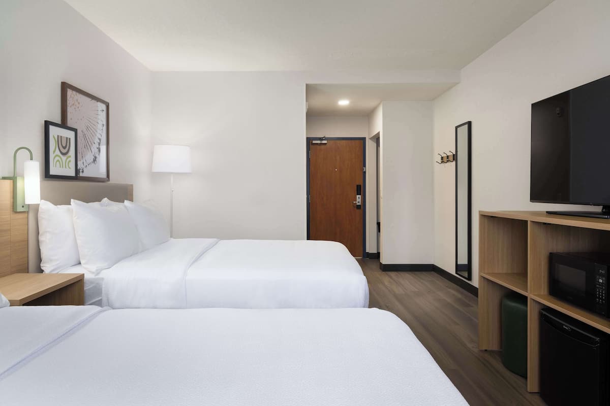 A hotel room with two beds, a TV, a microwave, and a wooden shelf.