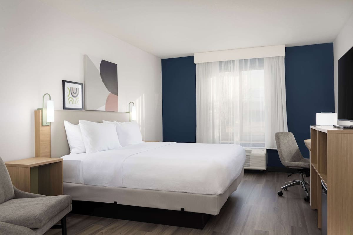 Relax in a spacious room with a large bed, wooden nightstand, and comfortable armchair.