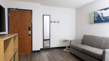 Una sala moderna con un sofá gris, un mueble bajo para televisión de madera, un espejo y una pequeña mesita auxiliar blanca.