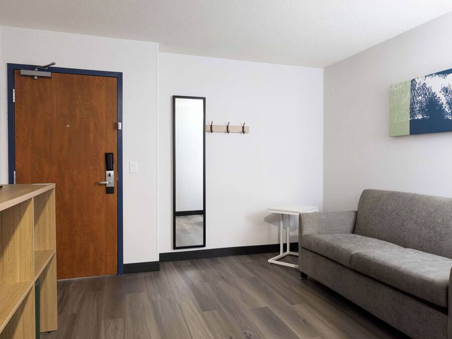 Una sala moderna con un sofá gris, un mueble bajo para televisión de madera, un espejo y una pequeña mesita auxiliar blanca.