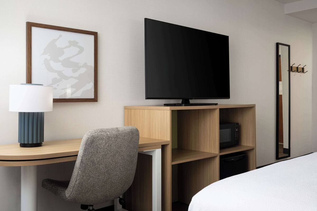 A hotel room with a bed, a desk with a chair, a television, a microwave, and a framed picture on the wall.