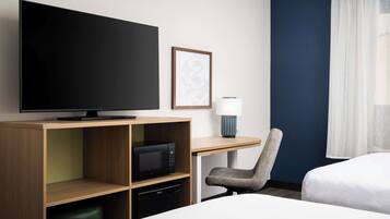 Habitación de hotel con cama, escritorio con computadora, televisor, microondas, silla y ventana con cortinas.
