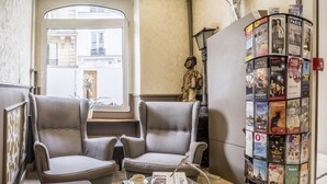 A cozy seating area with two armchairs and a small table, a magazine rack with travel brochures, and a window with a view of the street. - Chabrol Opéra (Paris)